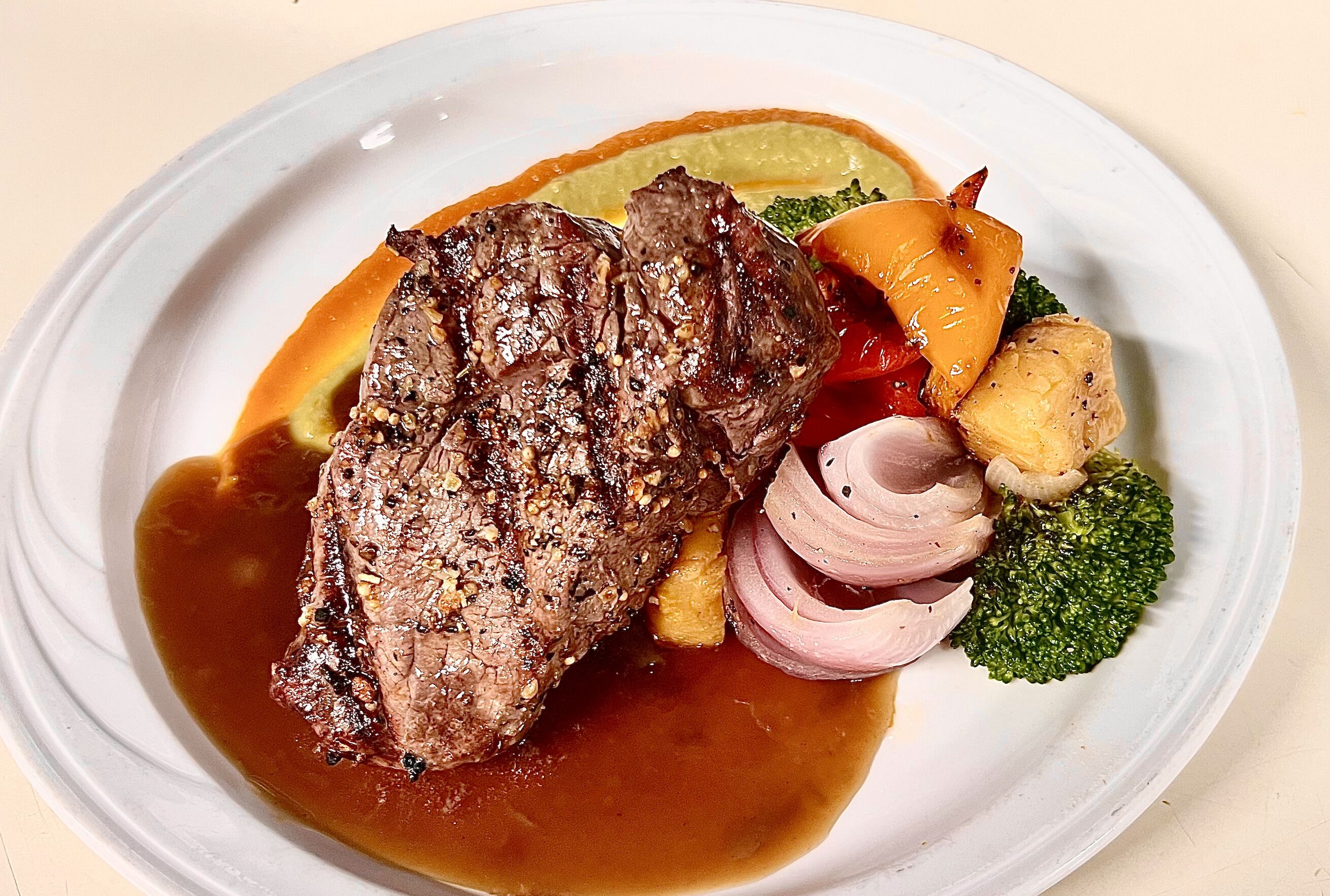 Ein Teller mit einem Steak, Gemüse und Soße.