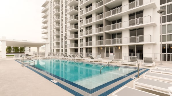 A swimming pool with lounge chairs and a multi-story building with balconies.