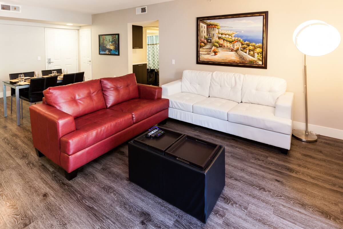 A living room with a red leather sofa, a white sofa, and a black coffee table. There is a painting on the wall and a floor lamp.