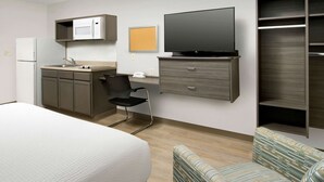 Una habitación de hotel con una cama, kitchenette, televisor, armario y un sillón a rayas.