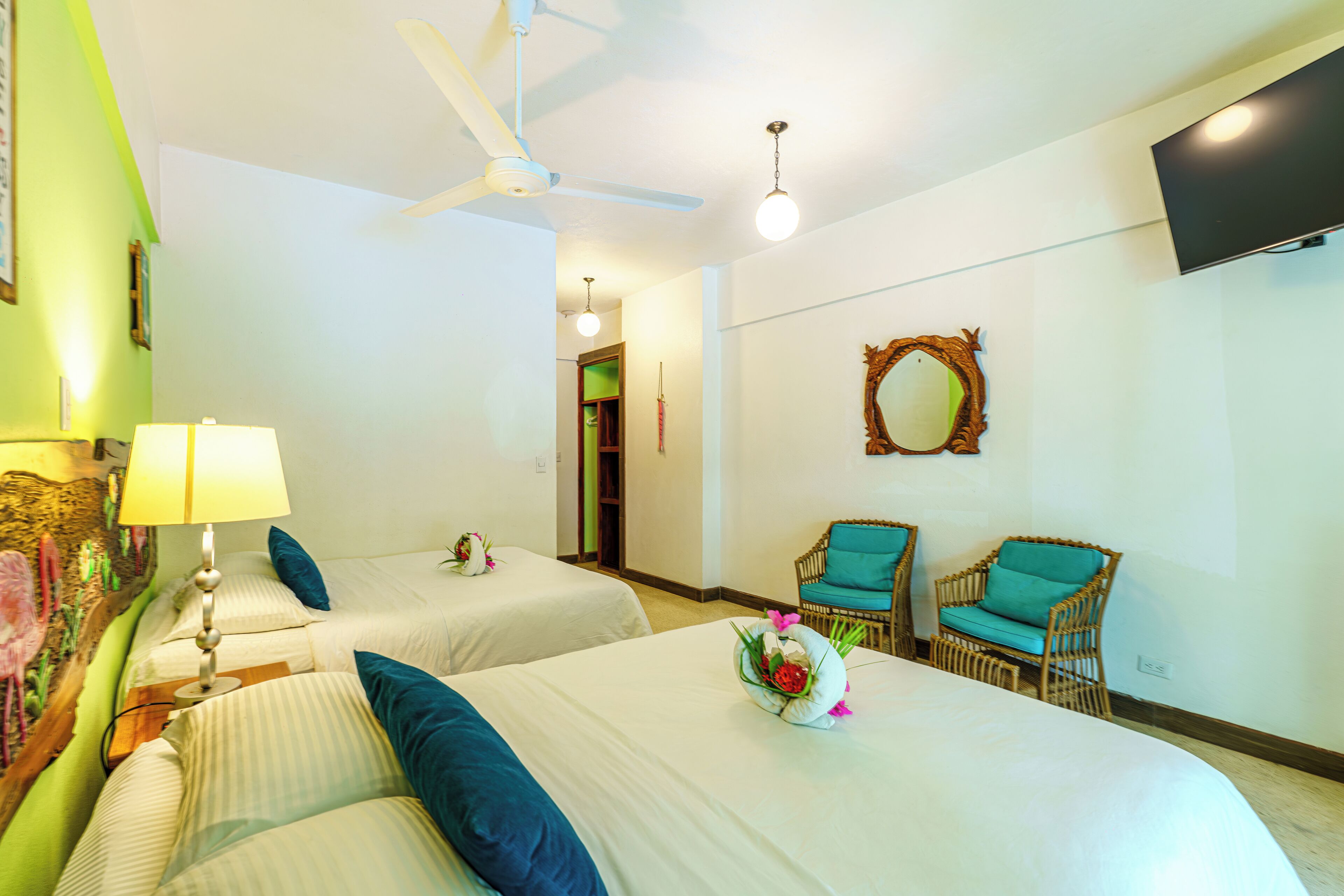A hotel room with two beds, a ceiling fan, a TV, and two wicker chairs.
