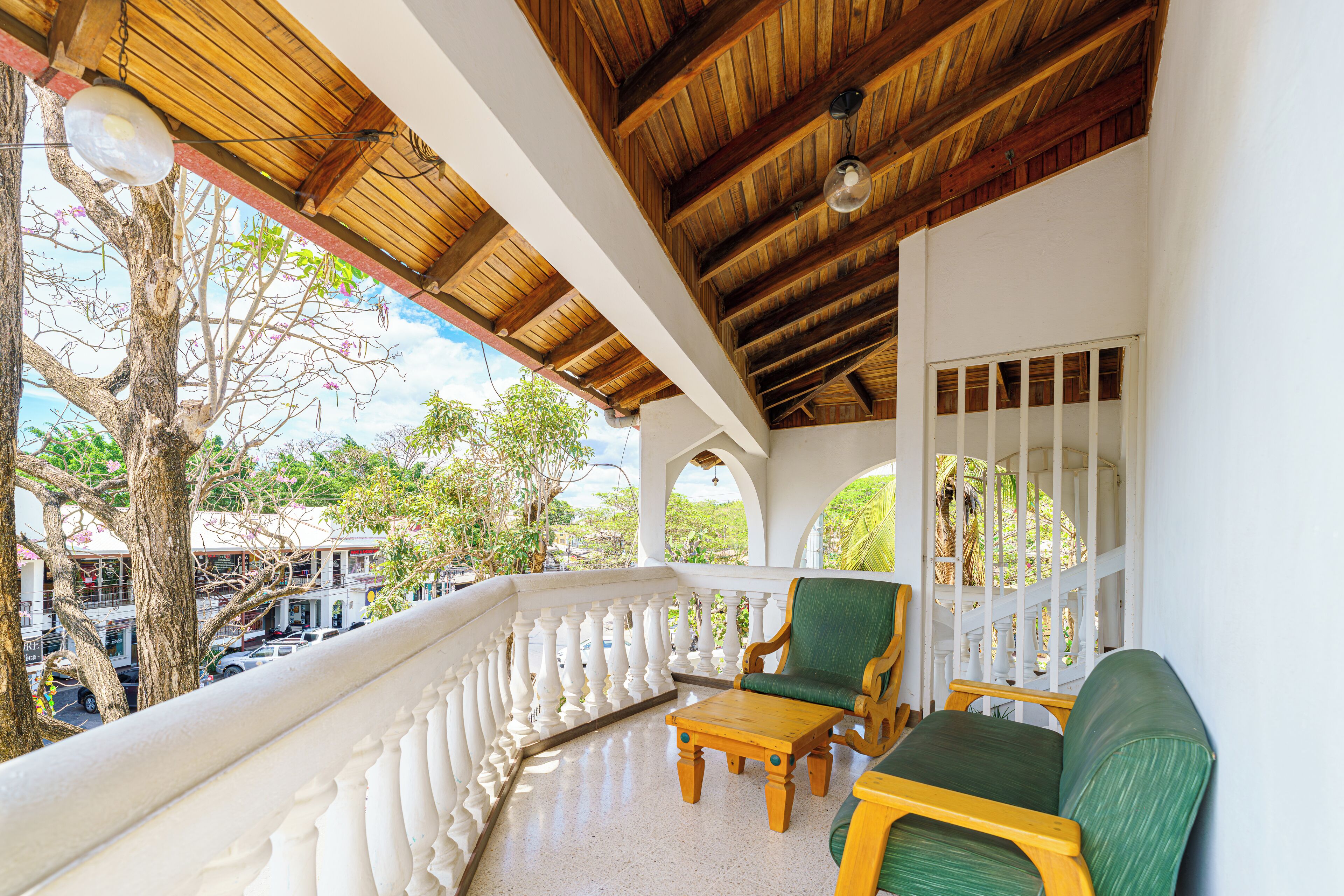 A covered balcony with a wooden ceiling, white balustrade, and a seating area with a table and chairs.