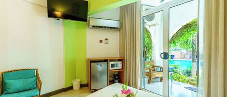 Une chambre d’hôtel comprenant un lit, une petite kitchenette, une télévision et donnant sur une piscine et un jardin.