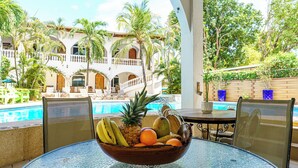 Uma área à beira da piscina com mesa, cadeiras e uma cesta de frutas.