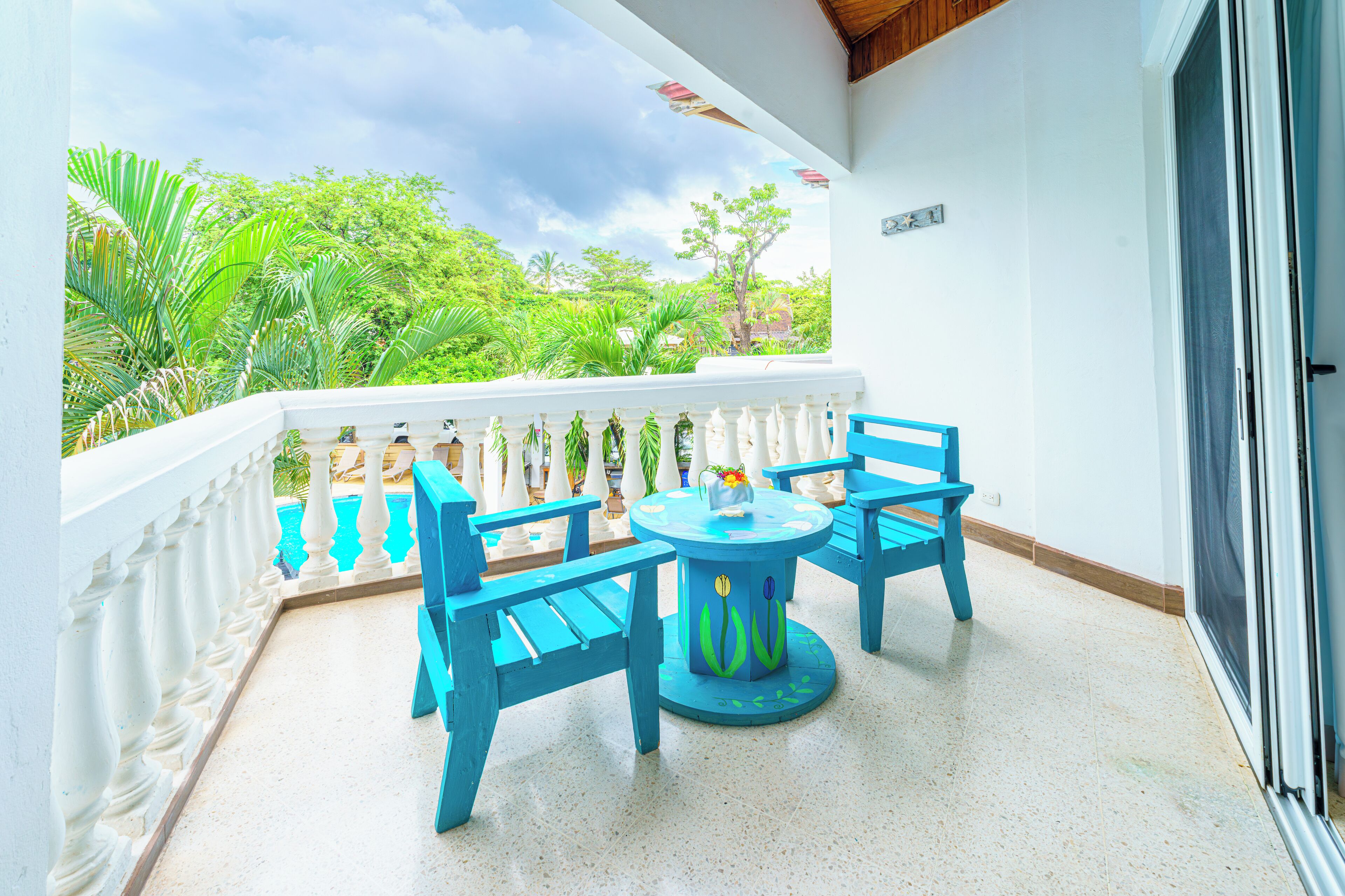 A balcony with a white railing, a round table with chairs, and a view of lush greenery.