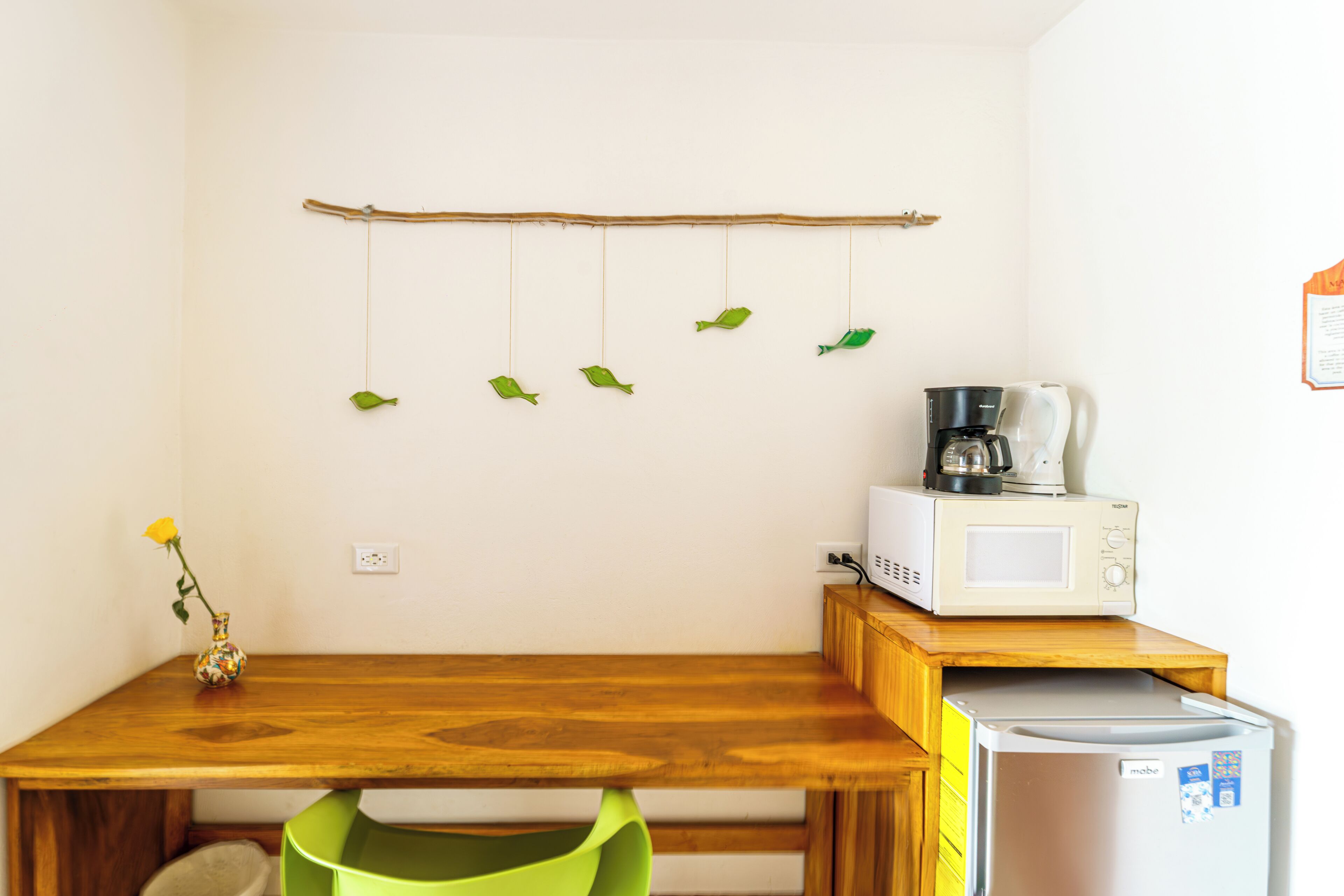 A kitchen with a wooden table, a microwave, a coffee maker, a refrigerator, and a hanging fish decoration.
