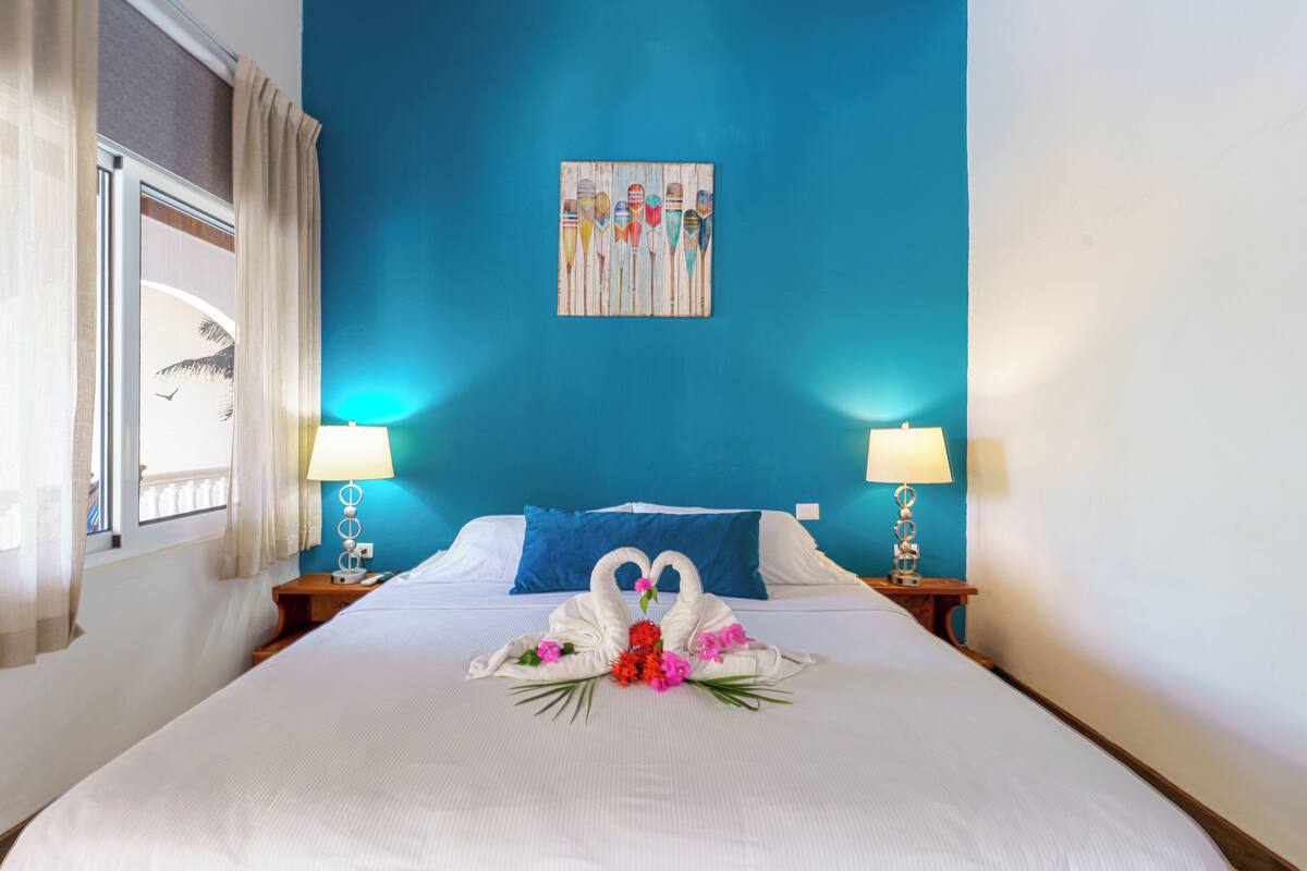 A hotel room with a bed, two bedside lamps, a blue wall, and a painting above the bed.