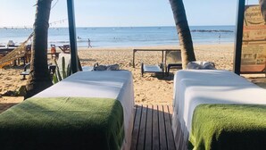 Quarto à beira-mar com duas camas, um deck de madeira e vista para a praia e o oceano.