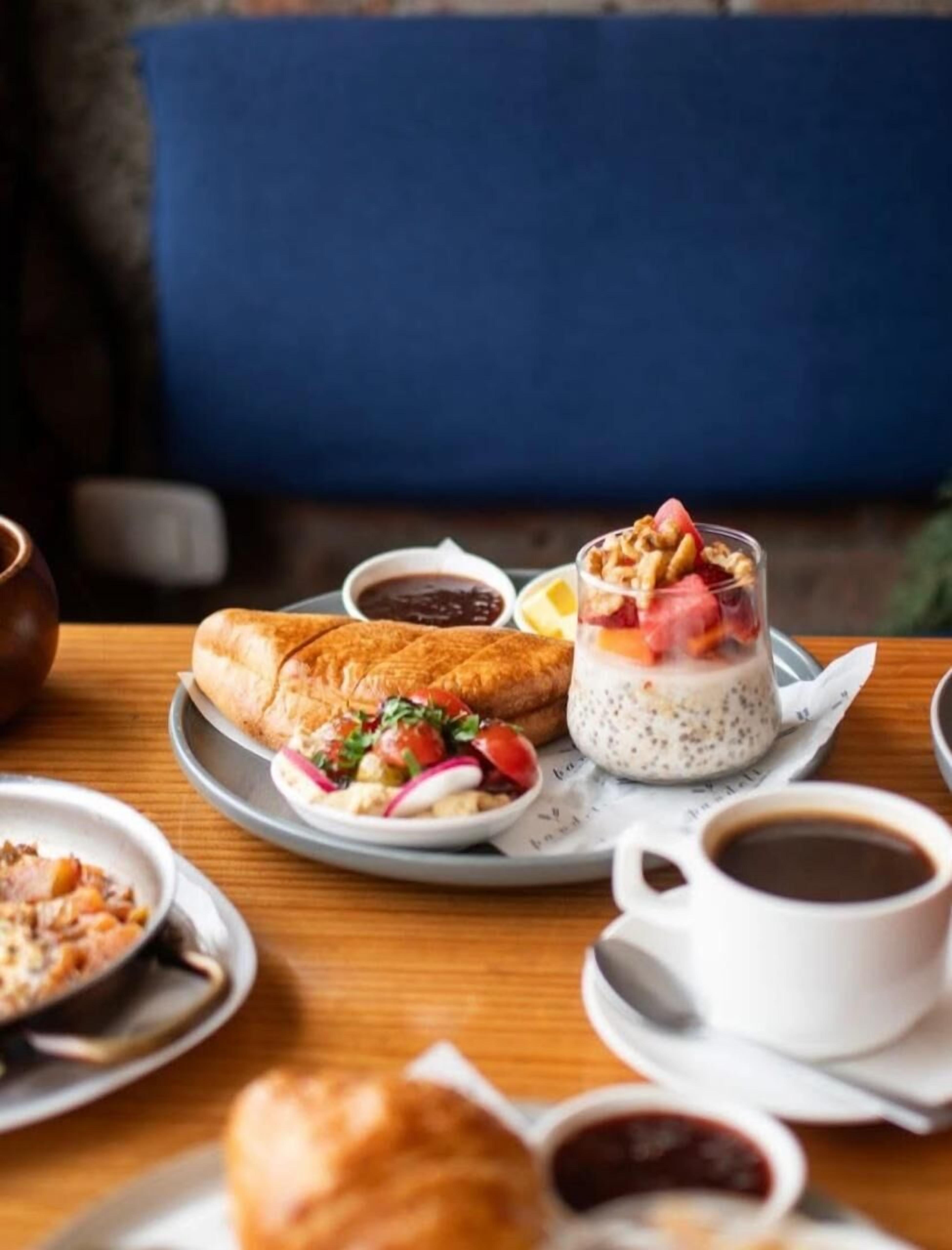 Une table dressée pour le petit-déjeuner avec un croissant, un dessert à plusieurs couches et une tasse de café, le tout présenté sur un plateau.