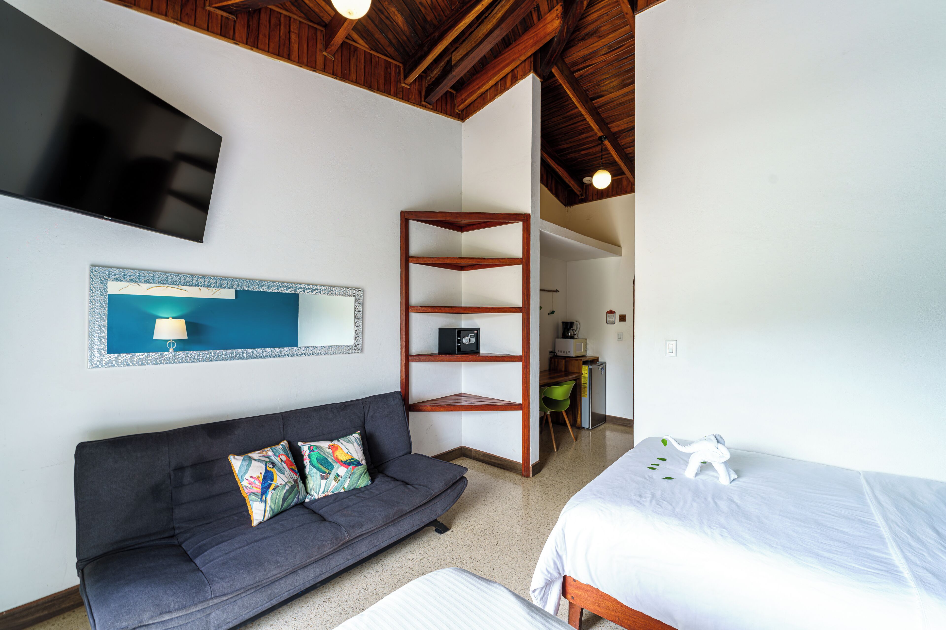 A room with a sofa, a bed, a TV, a shelf, and a desk.