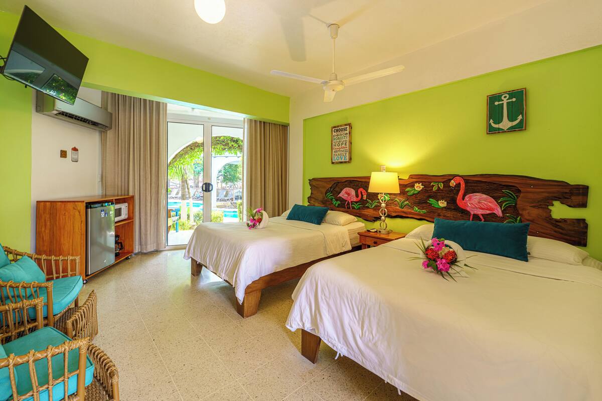 A hotel room with two beds, a desk with a refrigerator, a television, and a view of the outdoors.