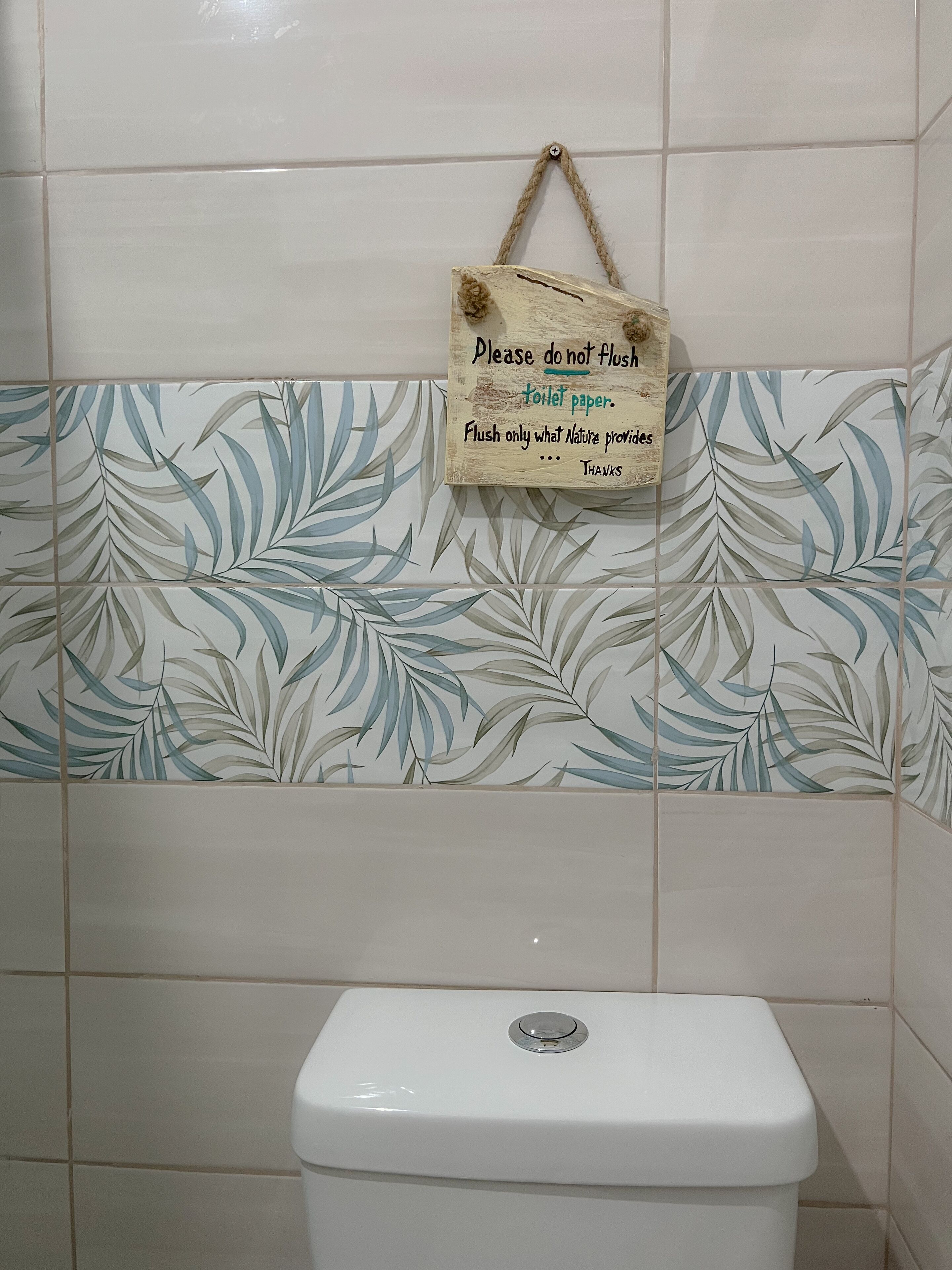A bathroom with a toilet, a sign on the wall, and a decorative leaf pattern on the tiles.