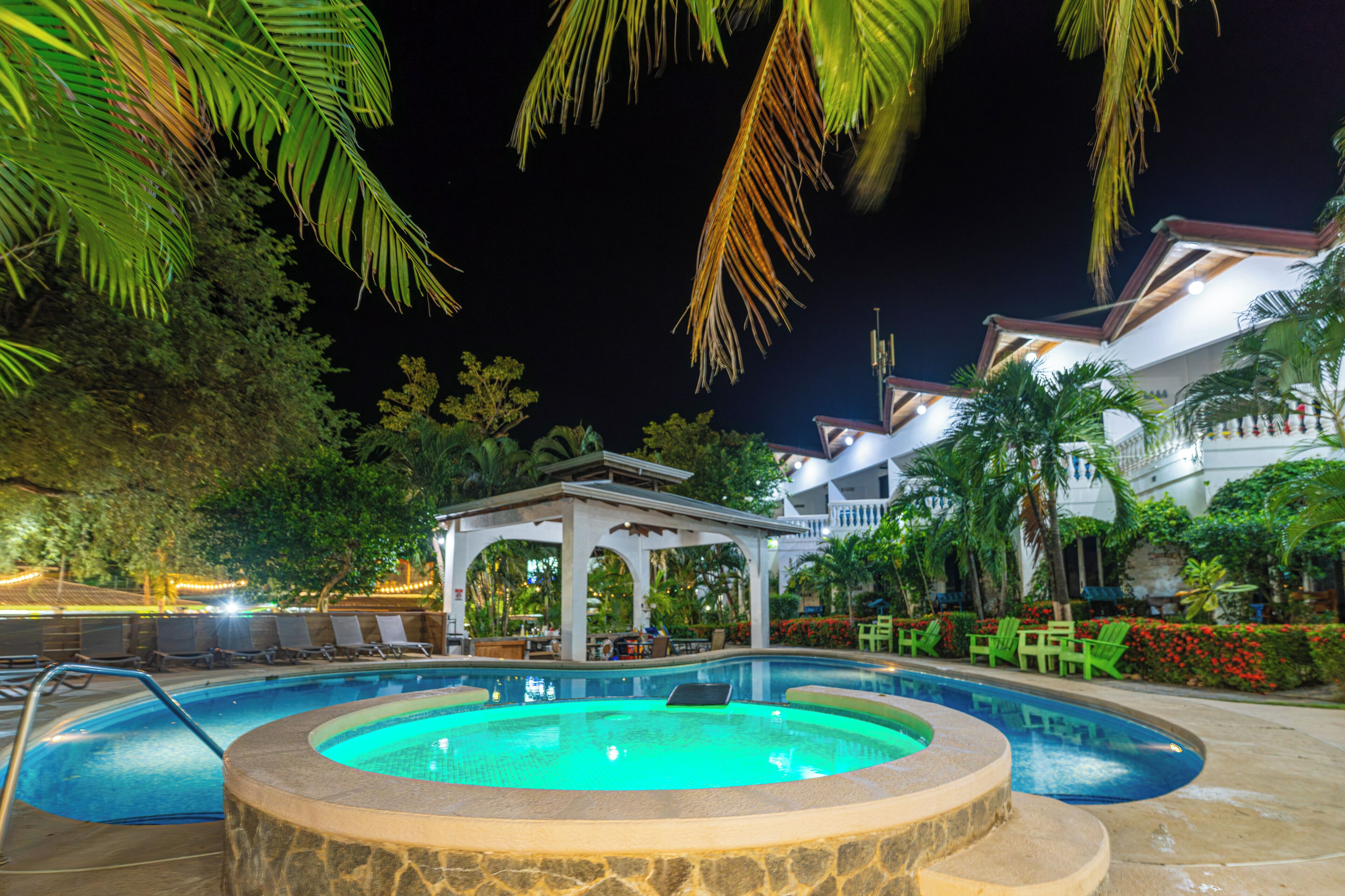 Una piscina con borde de piedra, rodeada de sillas de descanso y un pabellón.