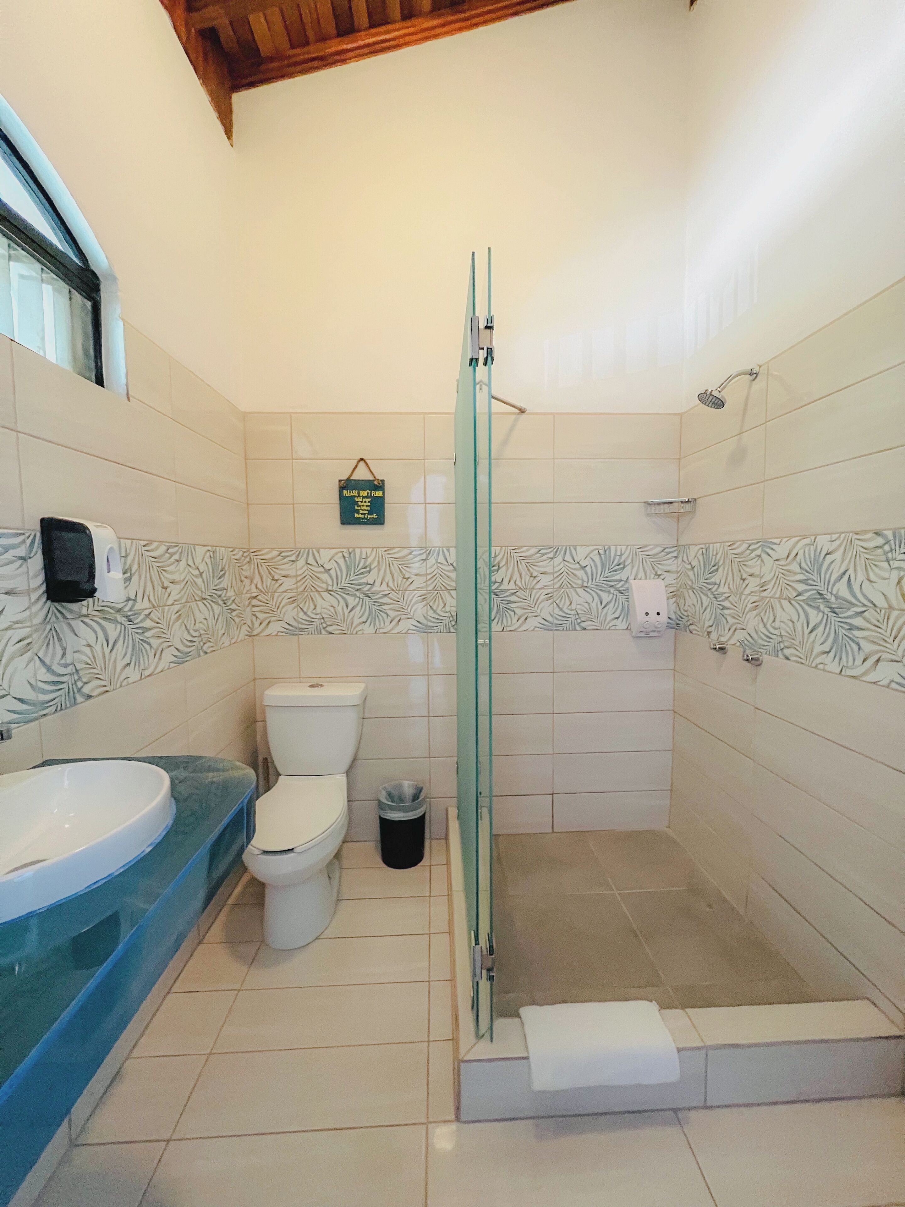 A bathroom with a glass-enclosed shower, a toilet, a sink, and a trash bin.