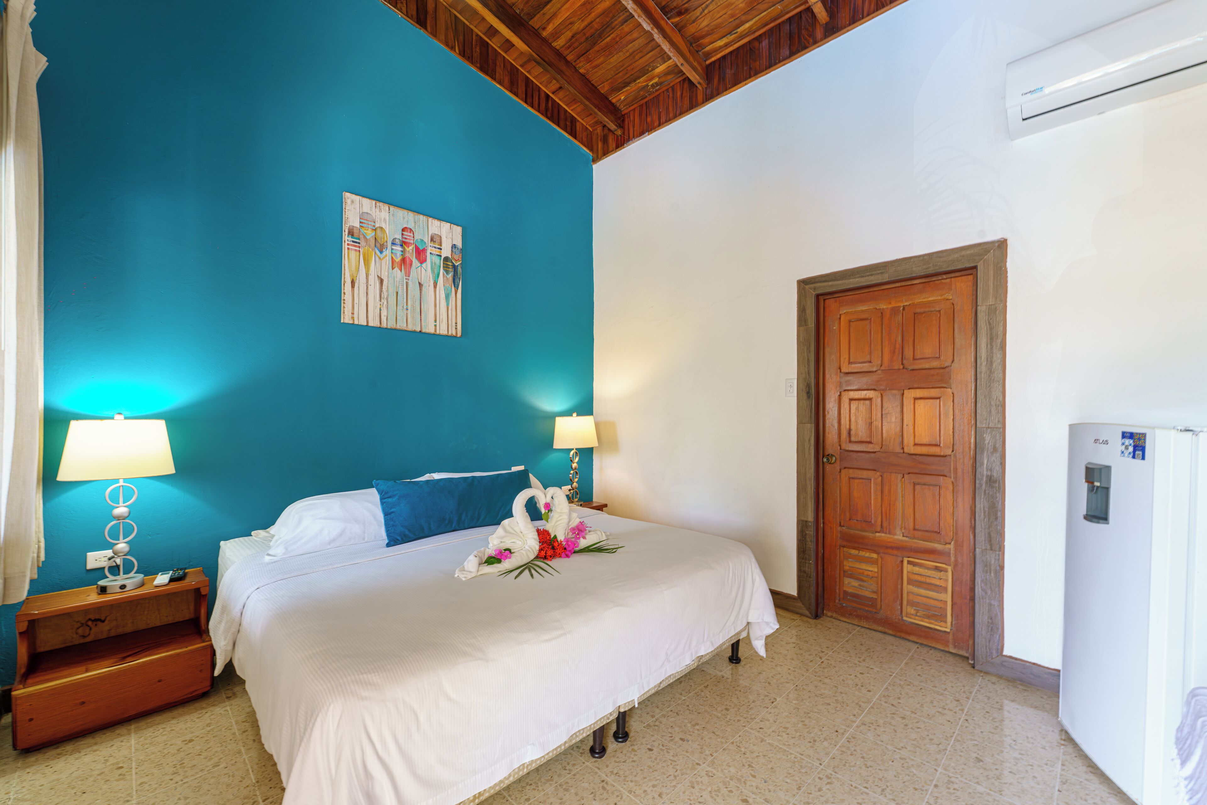 A bedroom with a bed, two bedside lamps, a wooden door, and a wall-mounted air conditioner.