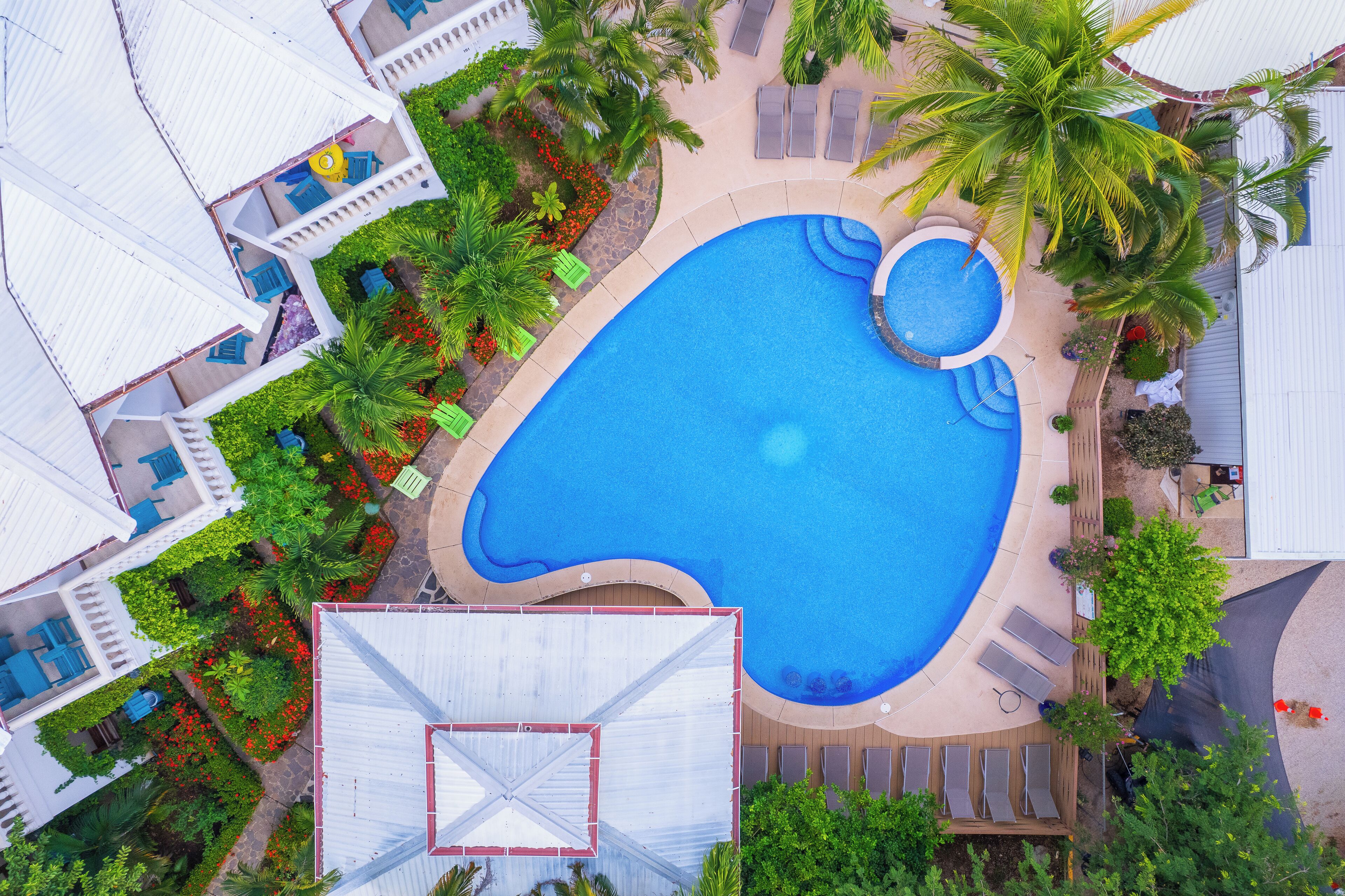An aerial view of a resort with a large swimming pool, multiple lounge areas, and lush landscaping.