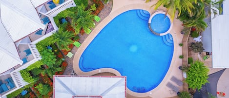 Vista aérea de un resort con una gran piscina, varias zonas de descanso y exuberante jardinería.