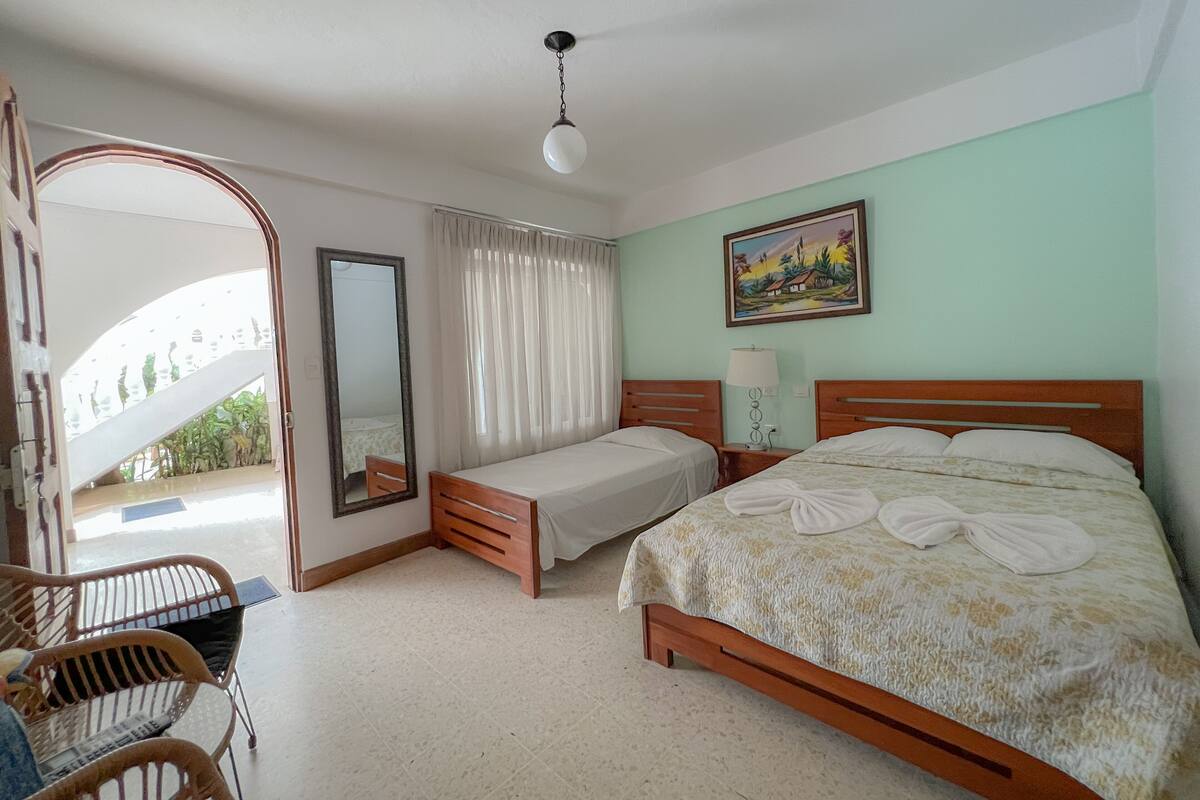 A hotel room with a bed, a chair, a desk, a mirror, and a painting on the wall.