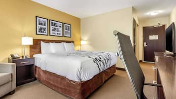 A hotel room with a bed, bedside table, lamp, chair, and a desk with a chair.