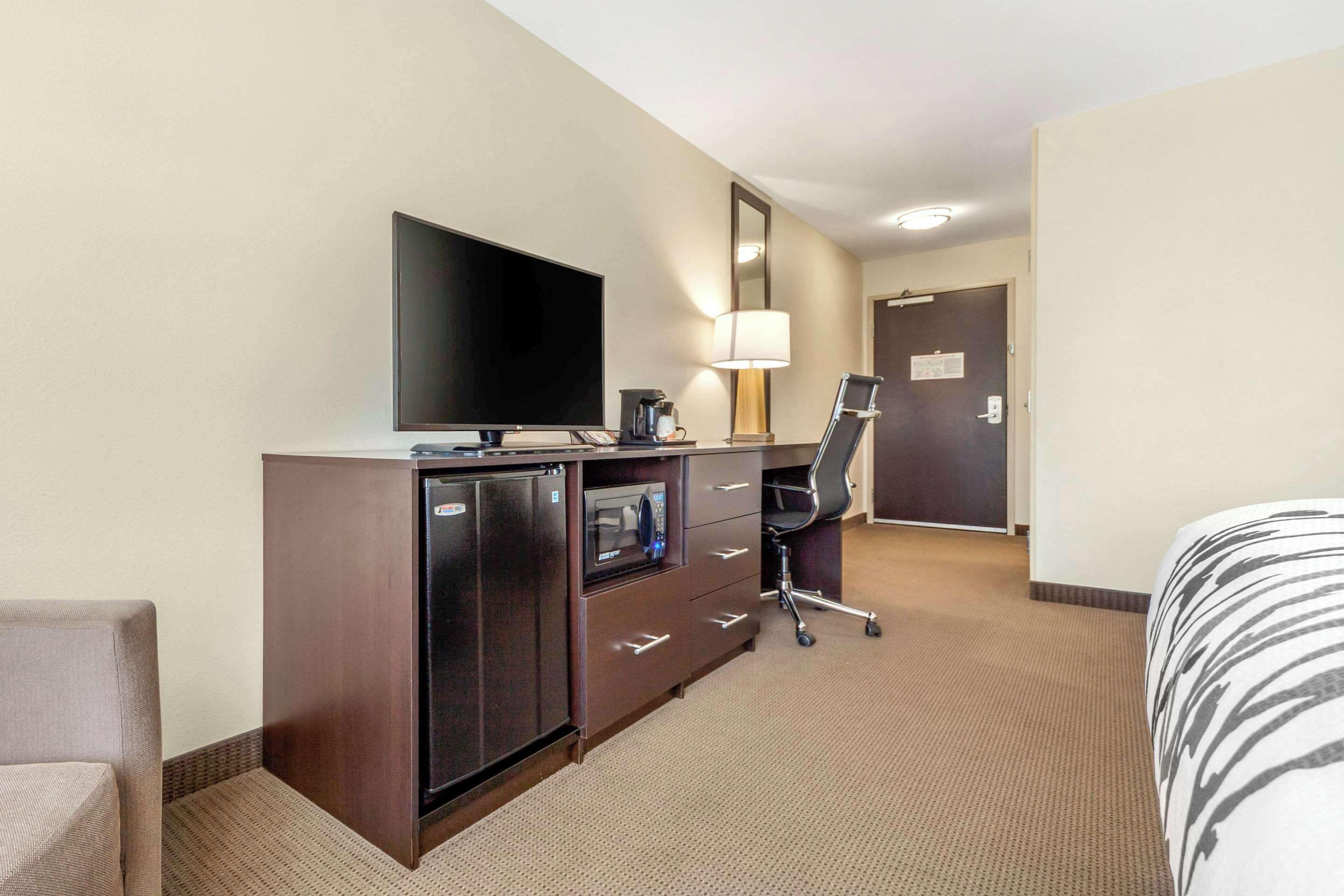 Habitación de hotel con televisión de pantalla plana, minibar, escritorio con lámpara, silla y cama.