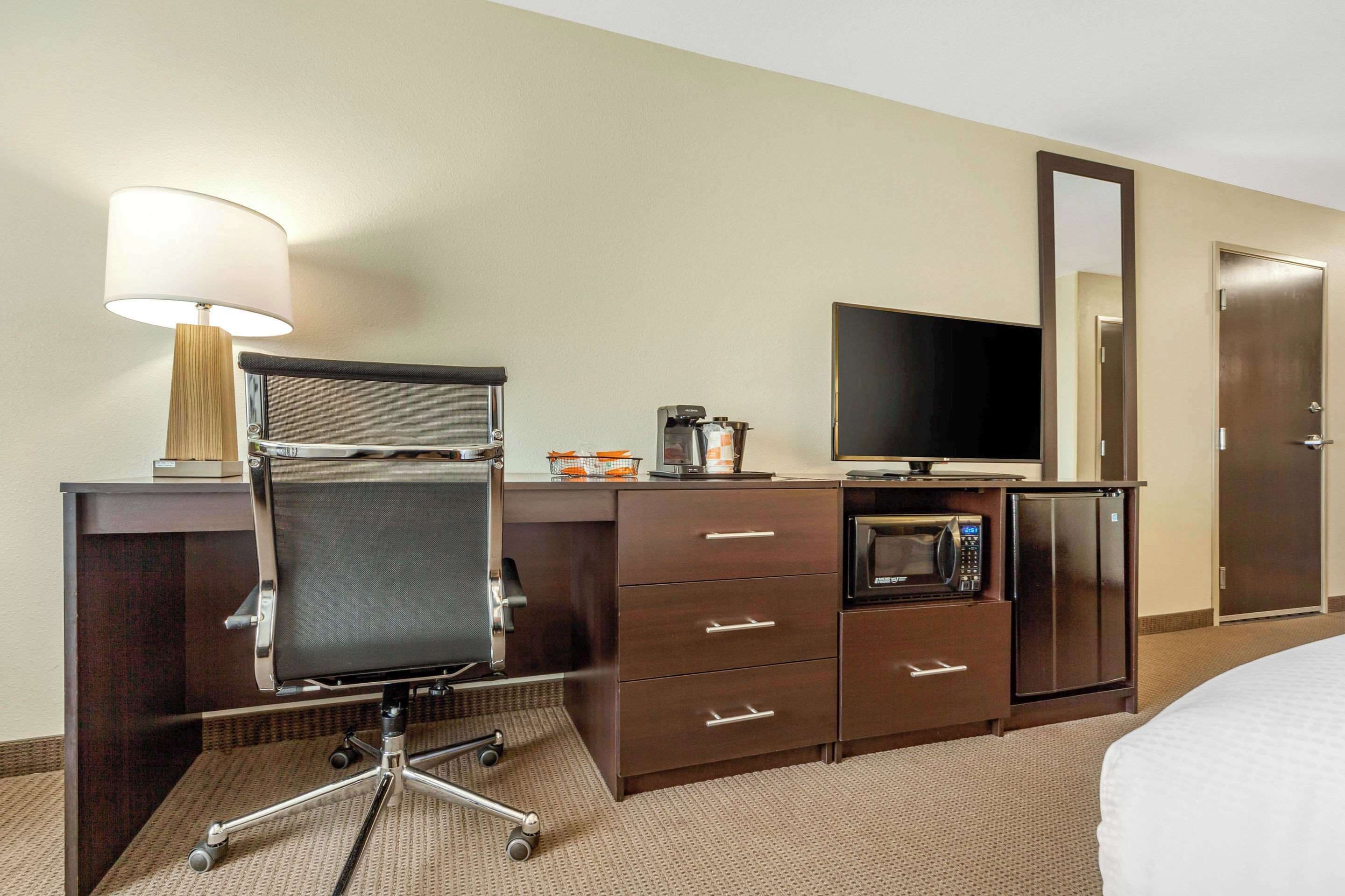 Ein Hotelzimmer mit Schreibtisch, Stuhl, Fernseher, Mikrowelle und einem Bett.