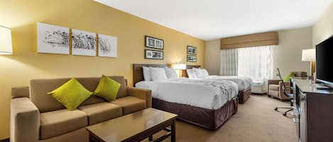 A hotel room with a sofa, two beds, a desk, and artwork on the walls.