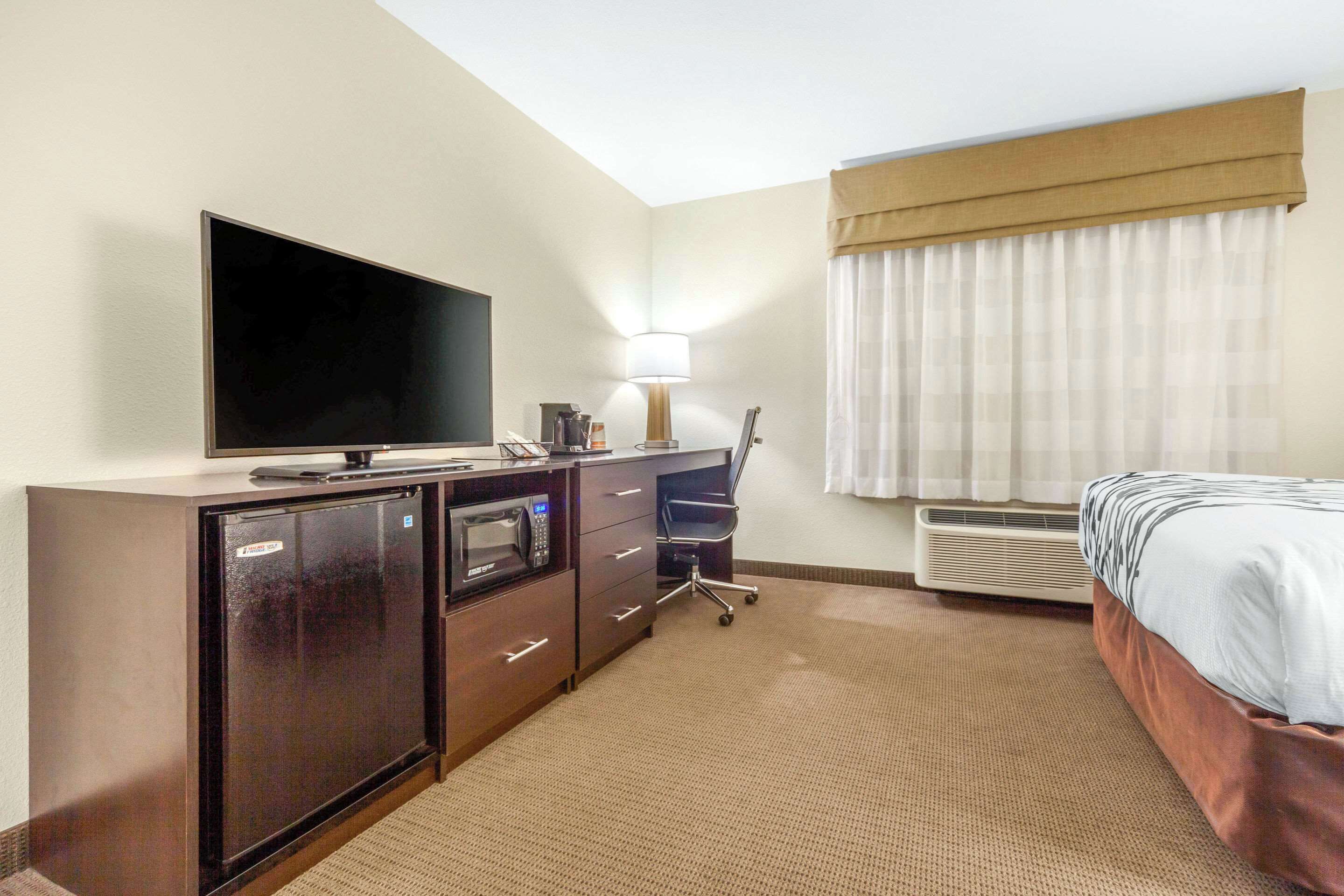Quarto de hotel com televisão de tela plana, uma escrivaninha com luminária, uma cadeira, uma cama e um ar-condicionado.