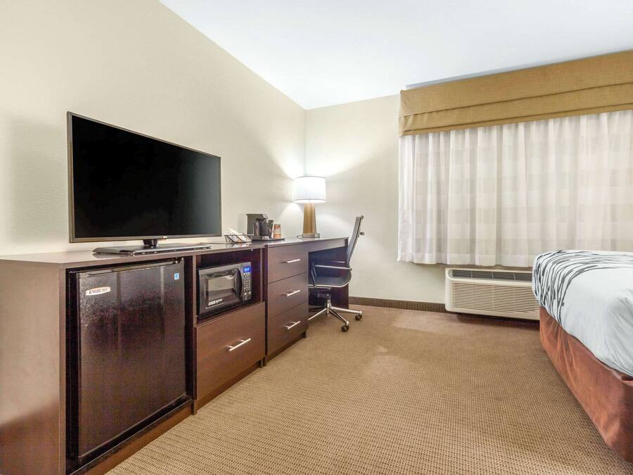 Habitación de hotel con televisión de pantalla plana, escritorio con lámpara, silla, cama y aire acondicionado.
