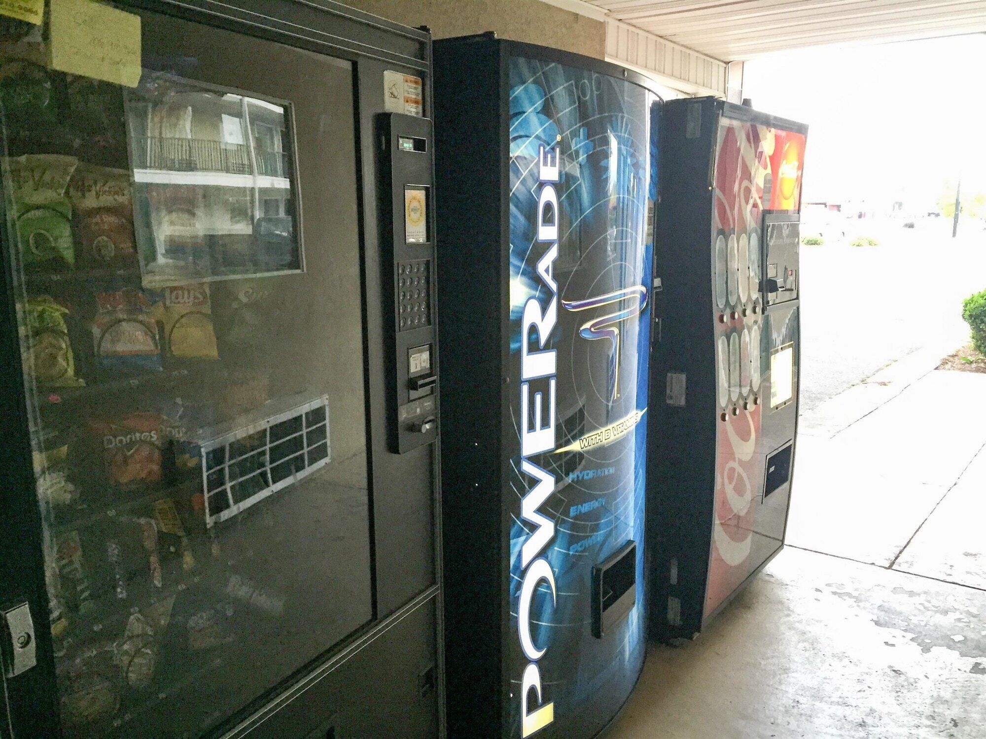 Drankenautomaten met een Powerade logo, een etalage met snacks, en een deur met een keypad.