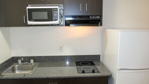 Una cocina con armarios oscuros, microondas, estufa, fregadero y refrigerador.