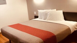 A neatly made bed with a red and beige bedspread, a wooden floor, and two wall-mounted light fixtures. - Motel 6 Augusta, GA - Fort Gordon (Augusta)