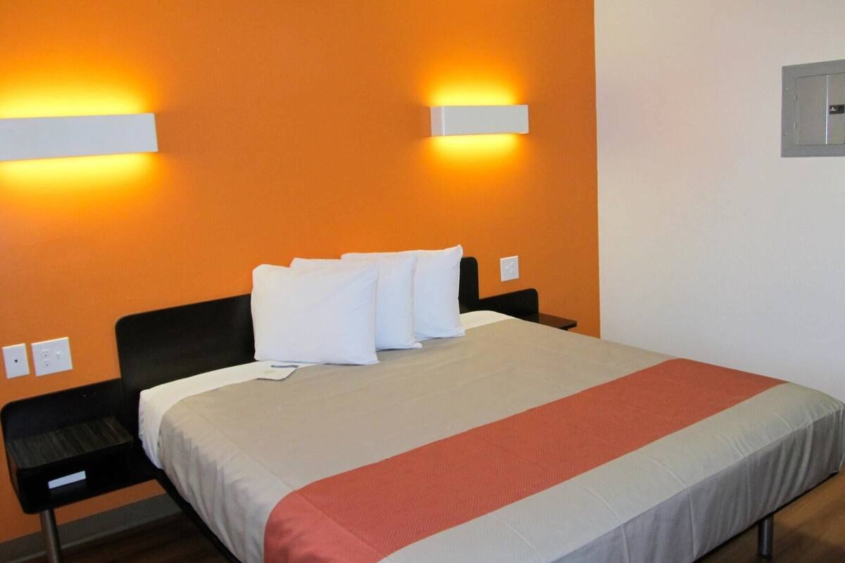 Hotellihuone, jossa on sänky, kaksi yöpöytää ja kaksi seinään kiinnitettyä valaisinta.