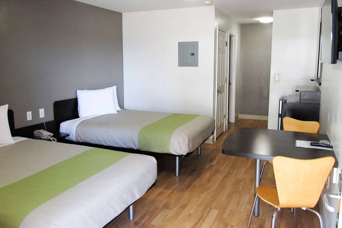 Hotellihuone, jossa on kaksi erillistä sänkyä, pieni pöytä, tuoli, työpöytä ja seinälle asennettu televisio.