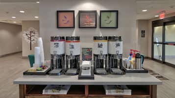 A coffee station with multiple coffee dispensers, a stack of disposable cups, and a sign indicating hot water and coffee options.