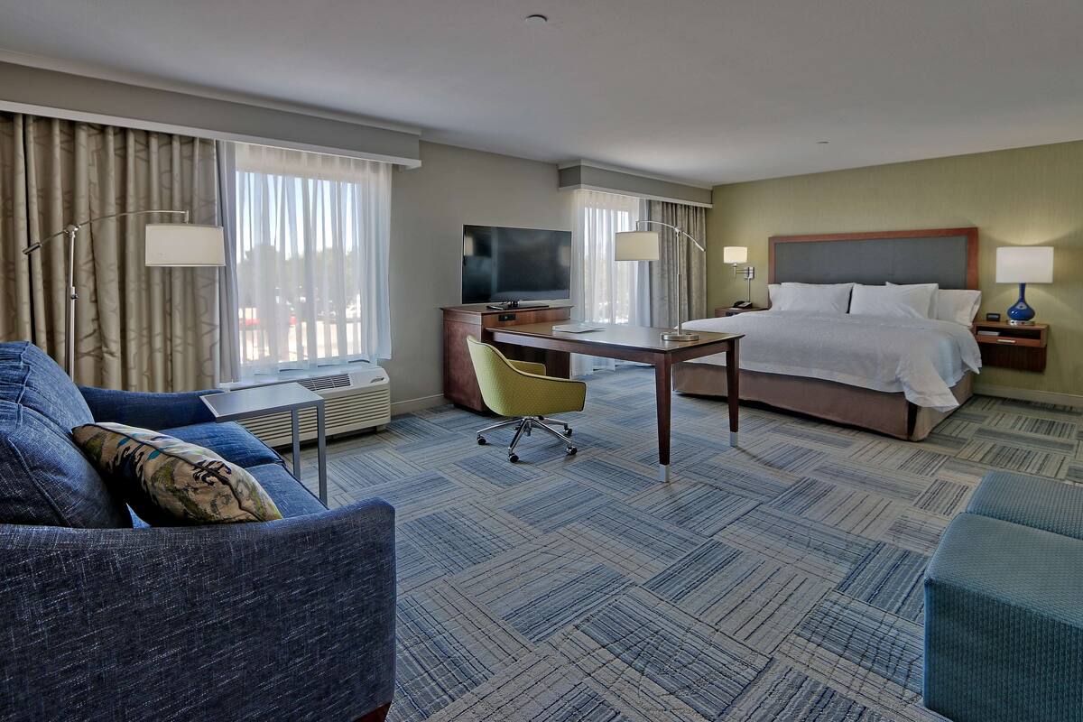 A hotel room with a bed, a desk, a chair, a TV, and a sofa.