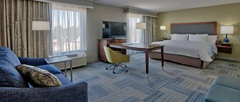 Una habitación de hotel con cama, escritorio, silla, televisor y sofá.