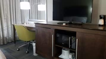 A hotel room with a desk, a television, a chair, and a minibar.