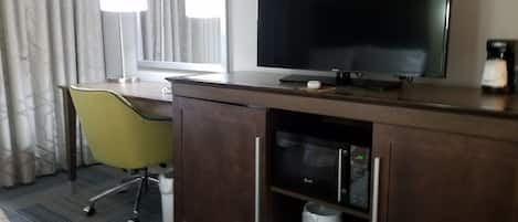 Una habitación de hotel con escritorio, televisión, silla y minibar.