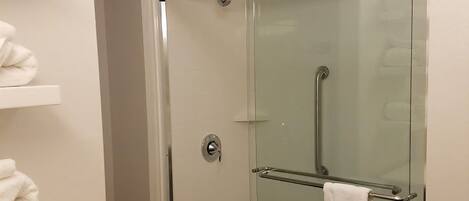 A glass-enclosed shower with a towel rack and a white towel hanging on it.
