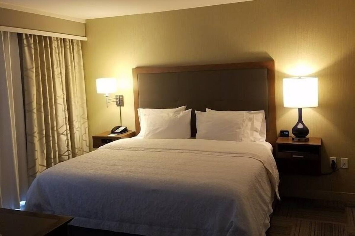 A hotel room with a large bed, two bedside tables with lamps, a wooden headboard, and a carpeted floor.