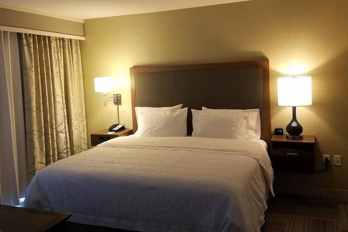 A hotel room with a large bed, two bedside tables with lamps, a nightstand, and a chair.