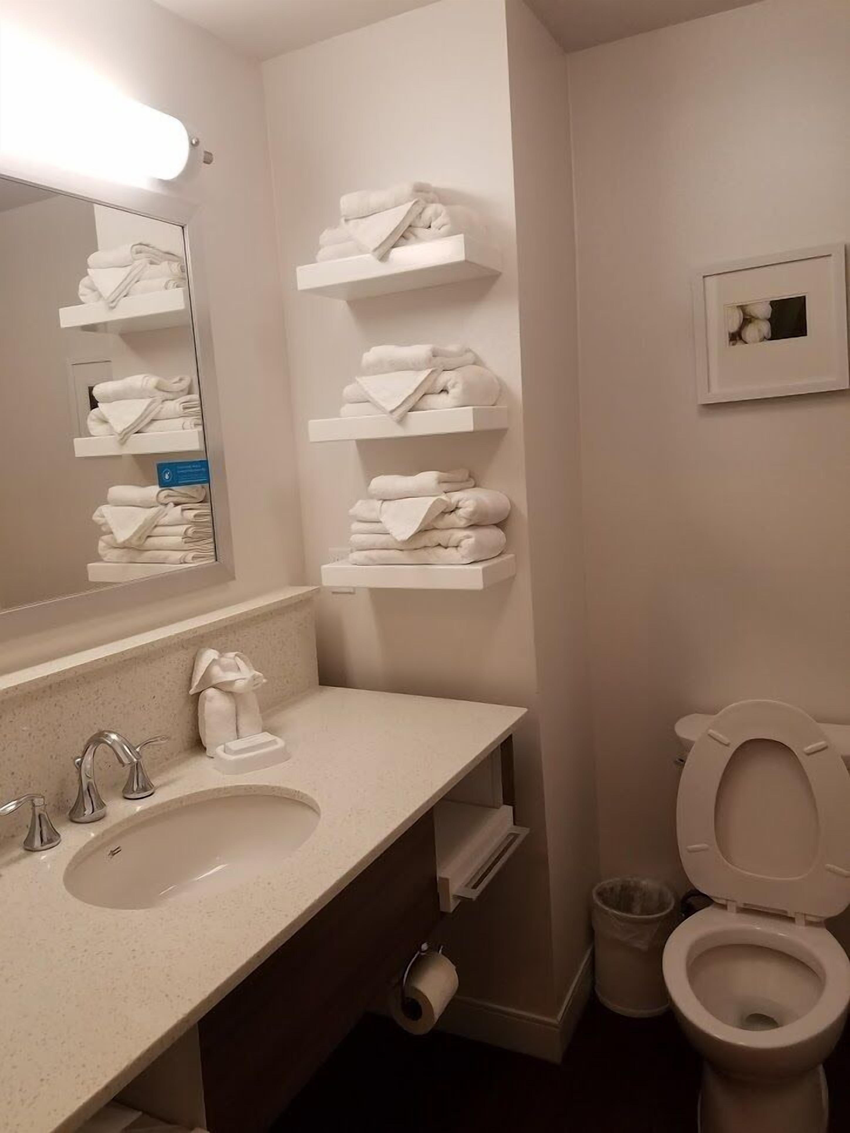 Un baño con lavamanos, espejo, toalleros, inodoro y un cubo de basura.
