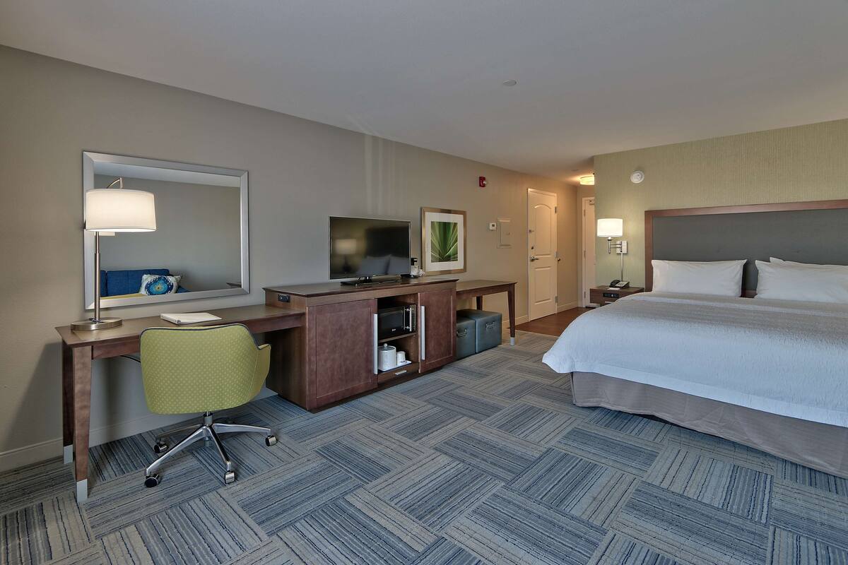 A hotel room with a bed, desk, chair, television, and a mirror.