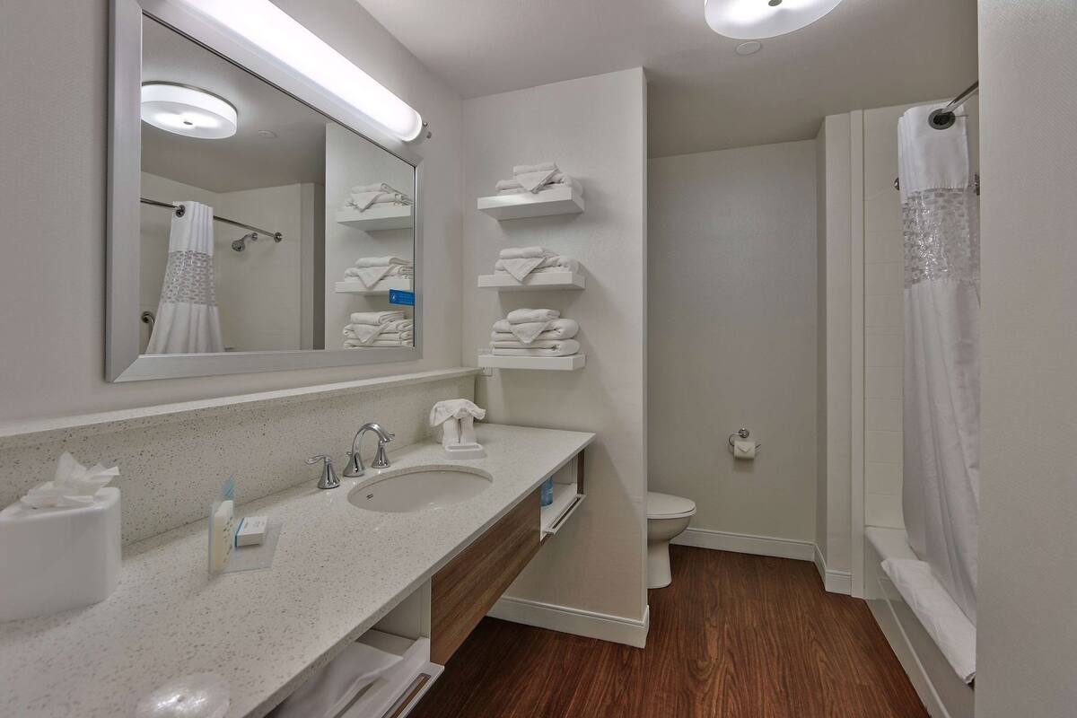 A modern bathroom with a double sink, a large mirror, a shower with a curtain, and neatly arranged towels.
