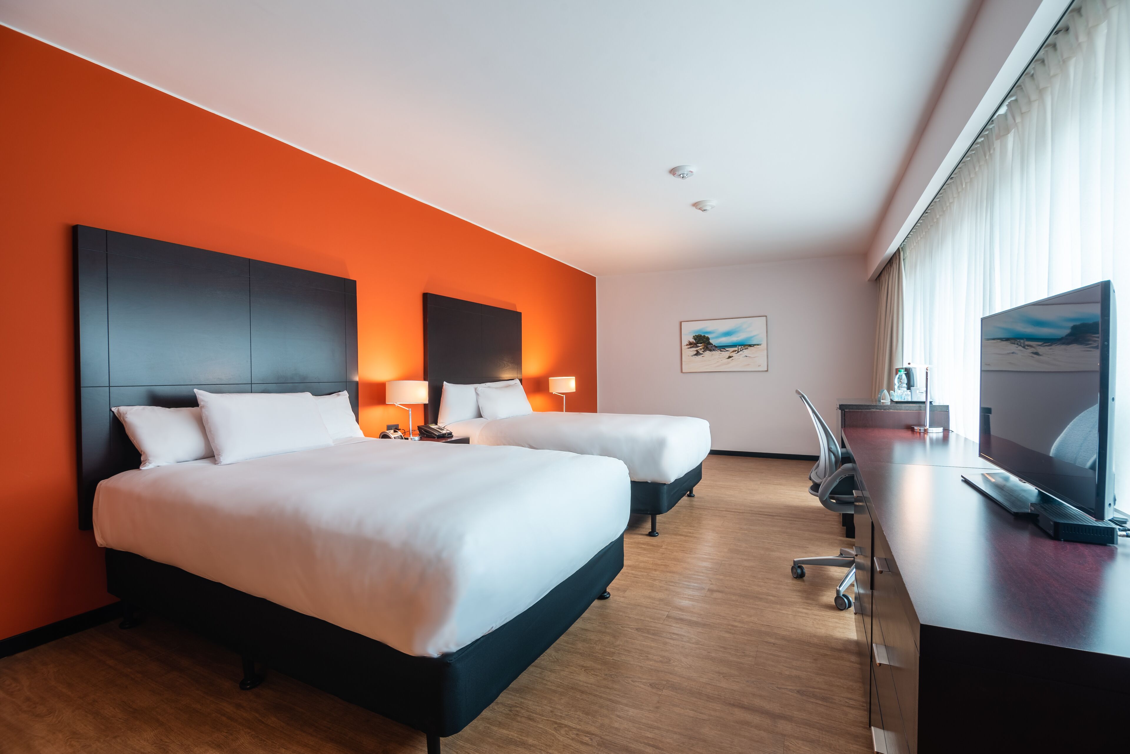Habitación de hotel con dos camas, un escritorio y un televisor.