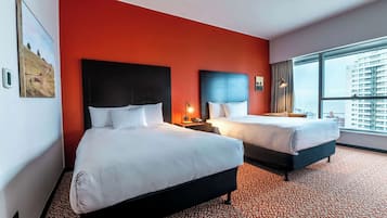 Habitación de hotel con dos camas, un muro decorativo rojo y un ventanal con vistas a la ciudad.