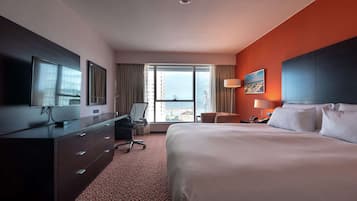 Habitación de hotel con una cama grande, un escritorio con silla, televisor y vistas a la ciudad desde la ventana.