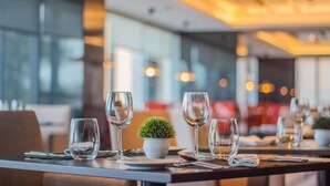 Une salle de restaurant avec des tables dressées pour le service, comprenant de la vaisselle en verre transparente et une petite plante en pot posée sur chaque table.