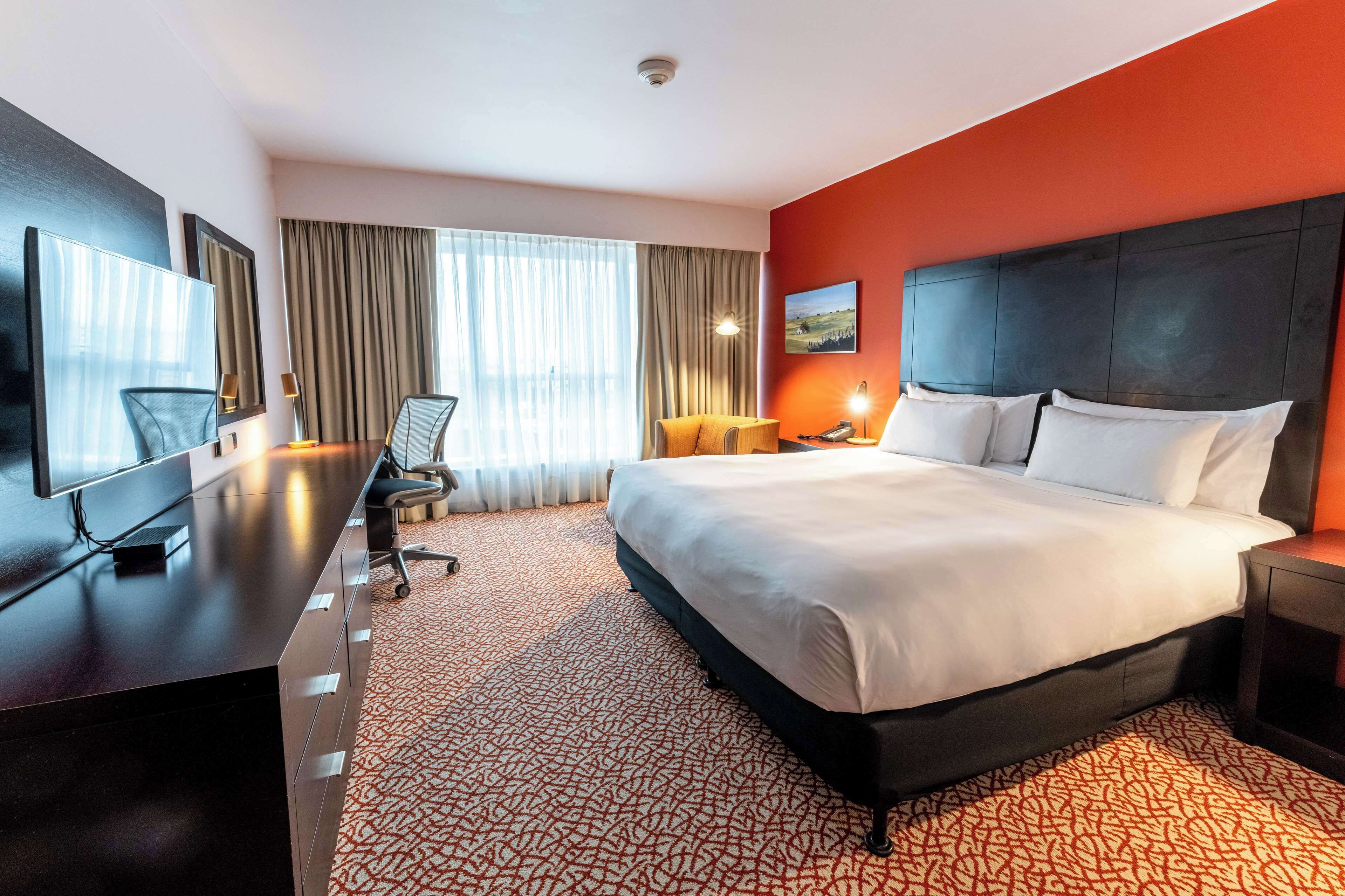 Una habitación de hotel con una cama grande, un escritorio con una silla, un televisor y un cuadro en la pared.