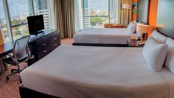 Habitación de hotel con dos camas, un escritorio con computadora y vistas a la ciudad.